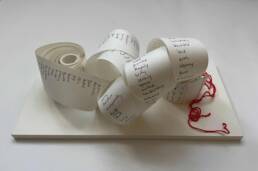 A spiral of till roll with handwritten words visible and red thread